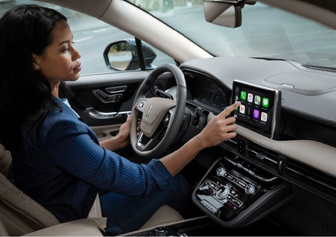 A woman in the driver's seat of a 2022 Lincoln Corsair is touching the center digital screen to connect to Apple CarPlay® | Performance Lincoln Bountiful in Bountiful UT
