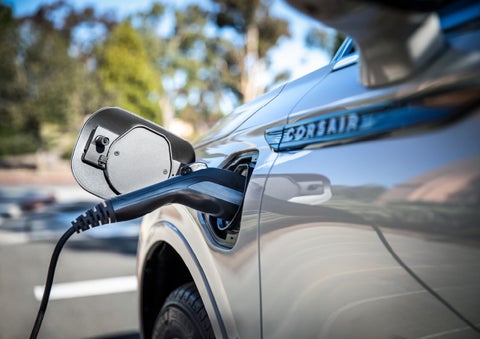 A Lincoln electric charger is plugged into a 2022 Lincoln Corsair Grand Touring port as the body reflects the surroundings of a sun-soaked parking lot | Performance Lincoln Bountiful in Bountiful UT