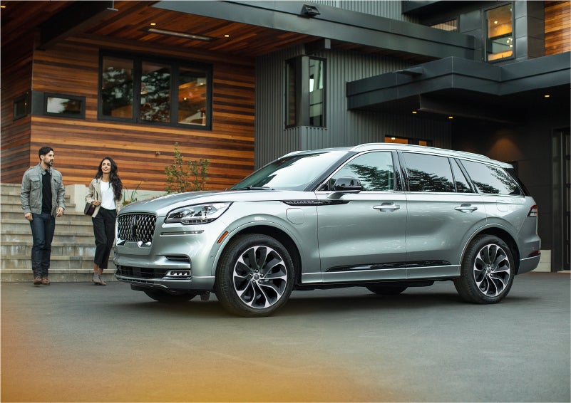 A couple approach a 2023 Lincoln Aviator® Grand Touring model parked in the driveway of a modern home | Performance Lincoln Bountiful in Bountiful UT