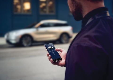 A person is shown interacting with a smartphone to connect to a Lincoln vehicle across the street. | Performance Lincoln Bountiful in Bountiful UT